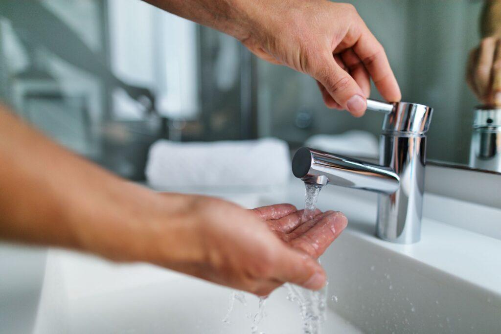 Person bedient eine moderne Bad-Armatur und lässt Wasser über die Hände fließen, um die hygienische Nutzung eines Wasserhahns zu demonstrieren.