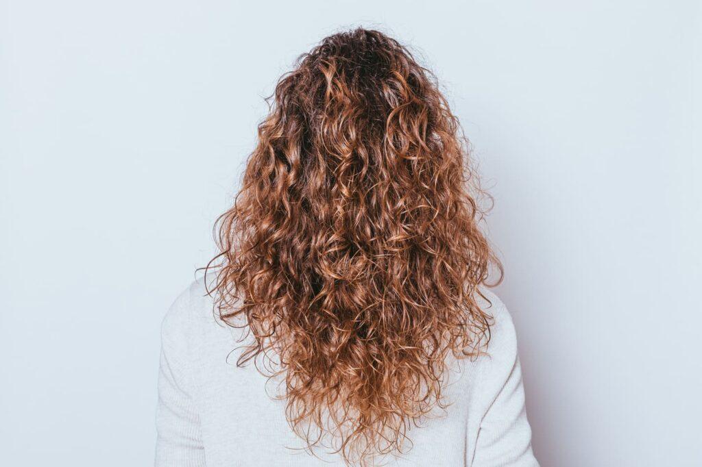 Rückansicht einer Frau mit langen, lockigen Haaren, ideal für die Verwendung von Ponytail Extensions.