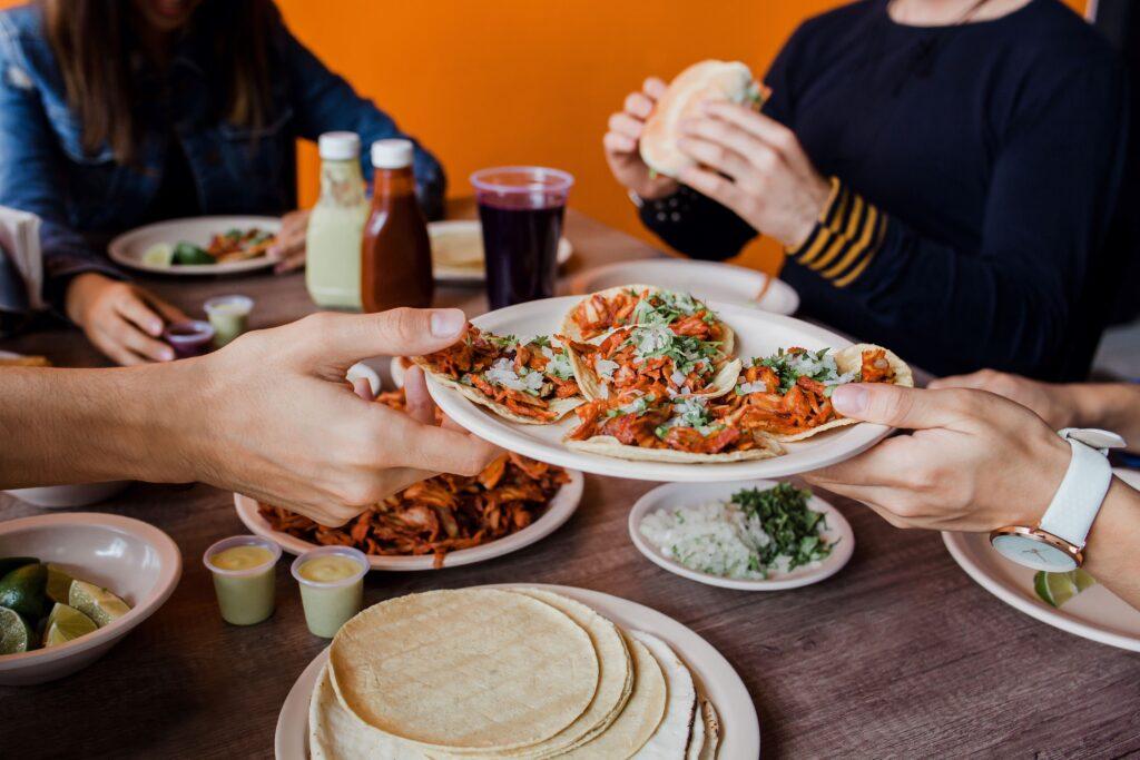 Personen teilen sich einen Teller mit frischen Tacos auf einem Tisch in geselliger Atmosphäre