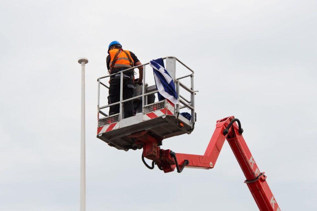 Arbeiter mit Helm und Sicherheitsweste nutzt Arbeitsbühne bei Wartungsarbeiten an Laterne im Freien