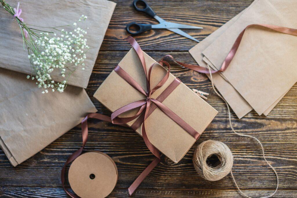 Geburtstagsgeschenk mit DIY-Verpackung aus Naturpapier, Schleifenband und Trockenblumen auf Holztisch