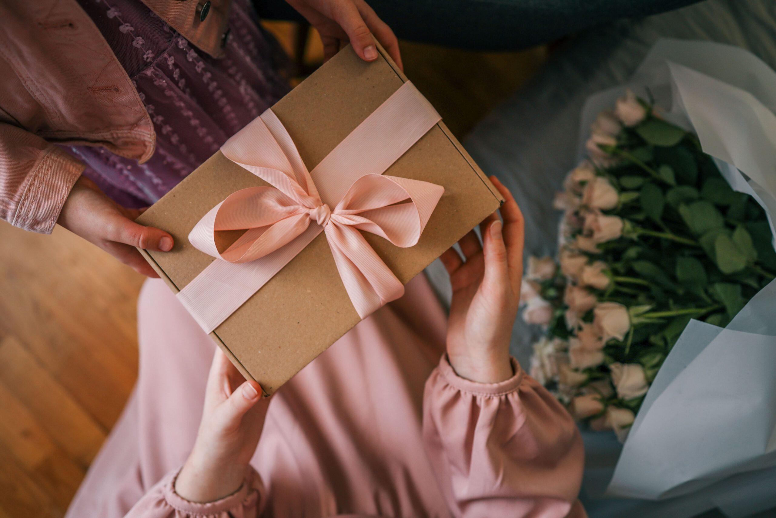 Zwei Personen überreichen sich ein Geburtstagsgeschenk mit rosa Schleife